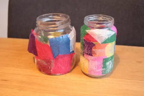 Twee glazen potjes, versierd met gekleurd papier en glitter, klaar voor kerst. Leuk om kerst potjes te maken!