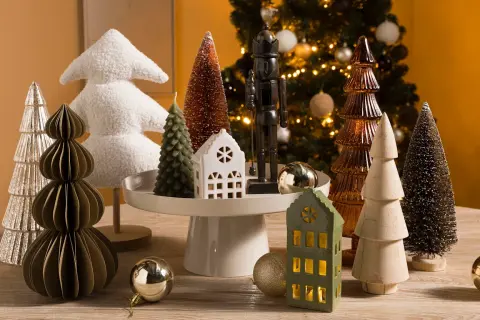 Kerstboom decoratie in Scandinavische stijl: diverse kerstboompjes, een notenkraker en huisjes op een houten tafel.