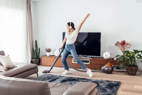 Vrolijke vrouw met koptelefoon danst tijdens de voorjaarsschoonmaak met de stofzuiger.