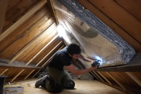 Man isoleert de zolder met reflecterend materiaal. Zo wordt de warmte in huis gehouden en bespaart hij op energiekosten.