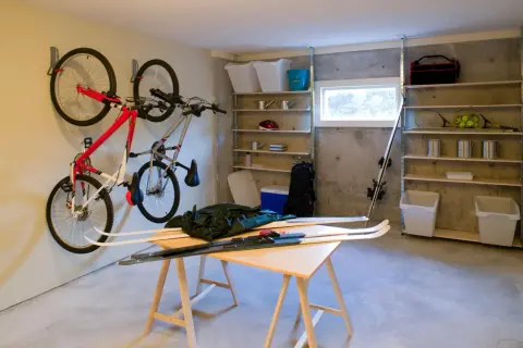 Een opgeruimde kelder met fietsen aan de muur, ski's op een tafel en opbergplanken vol spullen.