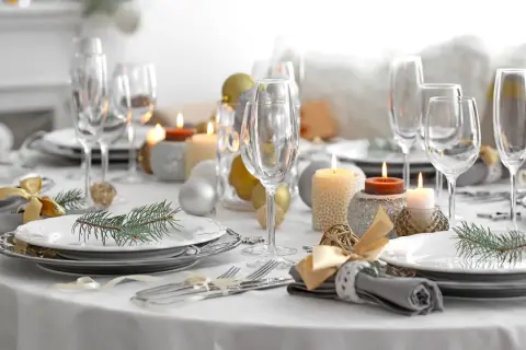 Een feestelijk gedekte tafel met glazen, kaarsen, kerstballen en dennentakjes. Klaar voor een gezellig diner!