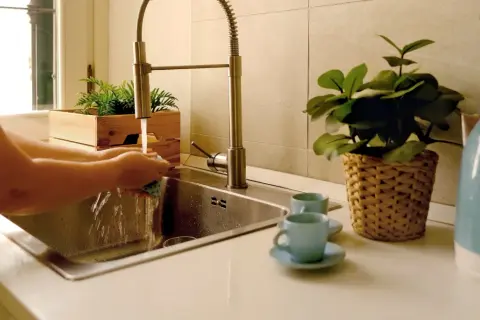 Iemand is bezig met het wasbak keuken schoonmaken. Water stroomt uit de kraan terwijl de handen een spons vasthouden.