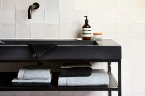 Stapel donkere handdoeken wassen en lichte handdoeken op een plank onder een zwarte wastafel.