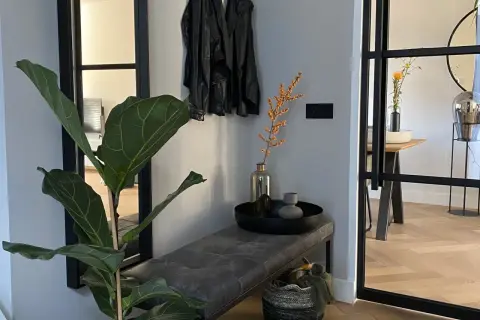 Een mooie hal met een grote plant, leren jasjes aan de kapstok, een bankje en een mand.
