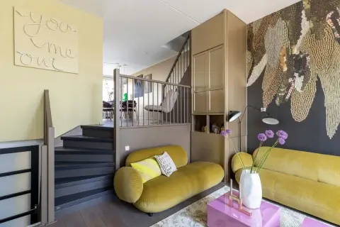 Gezellige split level woning met gele bank, trap en opvallende muurdecoratie.