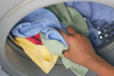 Hand pakt kleurrijke handdoeken en ondergoed uit de wasmachine.