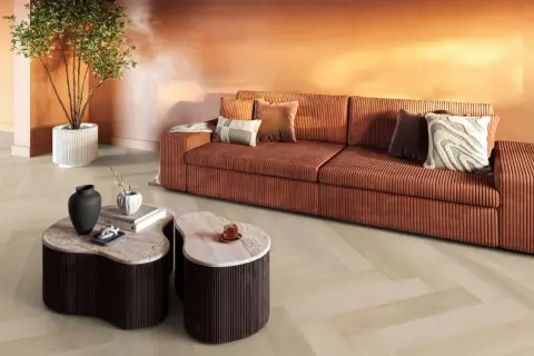 Een woonkamer met een oranje bank, marmeren tafels en een plant. De lichte evc vloer met visgraatmotief vormt een rustige basis.