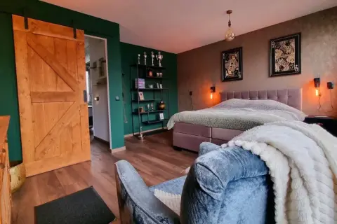 Slaapkamer met groene muur, houten schuifdeur en een bed met een deken met een subtiel ombre effect.