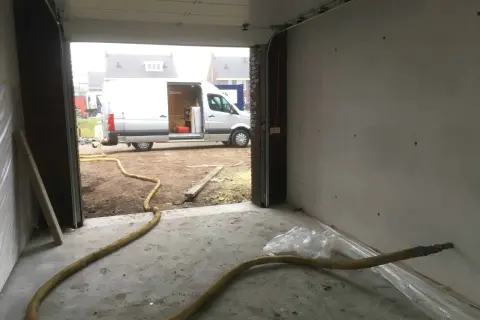Grote gele slang voor zand stralen in een garage, met een busje buiten.