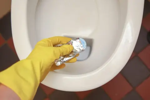 Gele handschoen houdt product vast om kalkrand wc pot te verwijderen.