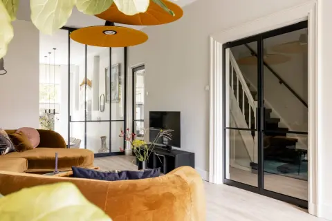Gezellige woonkamer met oranje bank, glazen deuren naar de trap en een ontspullen lijst.