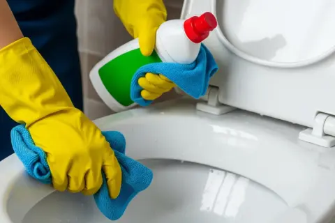 Gele handschoenen maken de wc vloer schoon met een blauwe doek en schoonmaakmiddel.