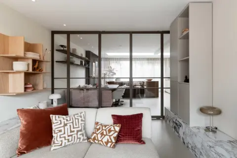 Moderne woonkamer met glazen wand, houten wandrek en comfortabele bank. Een nis in de muur is stijlvol ingericht.