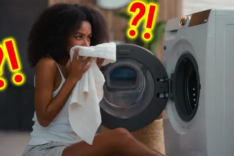 Vrouw ruikt aan een handdoek bij een wasmachine. Vraagt zich af hoe vaak handdoek gebruiken? Grote rode vraagtekens suggereren twijfel.