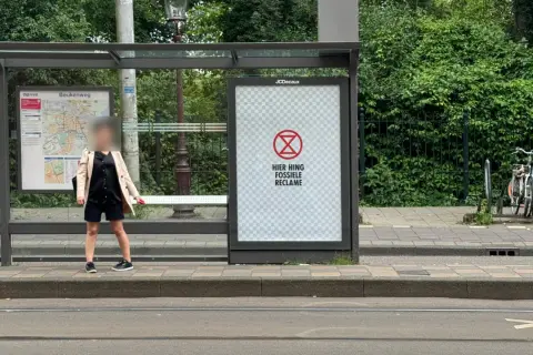 Een poster bij een bushalte met een symbool en de tekst "HIER HING FOSSIELE RECLAME". Dit is een oproep om geadresseerde reclame stopzetten.