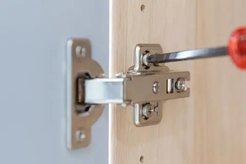 Met een schroevendraaier worden twee schroeven van een scharnier bijgesteld om de kastdeur perfect te laten sluiten.