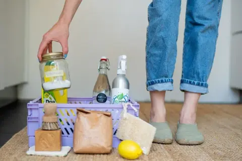 Een mand met spullen voor duurzaam schoonmaken: citroenzuur, azijn, zeep, borstel, citroen en een loofah.
