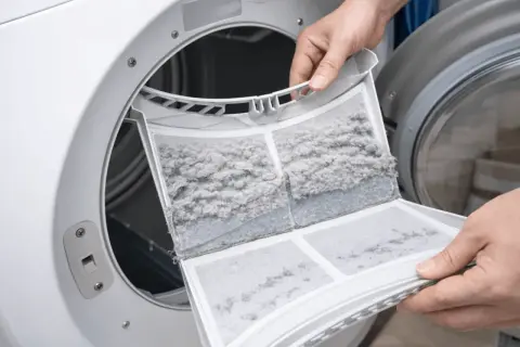 Een verstopte pluizenfilter van de wasmachine, vol met grijze pluisjes. Dit kan leiden tot een wasmachine die vastloopt.