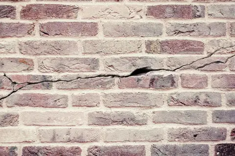 Een oude bakstenen muur met duidelijke scheuren die door de stenen lopen, getuigen van de tand des tijds.