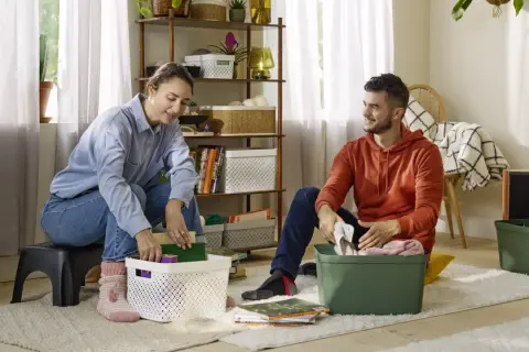 Een stel pakt spullen in, klaar voor hun reis van ontspullen in 52 weken. Ze sorteren boeken en kleding in opbergbakken.