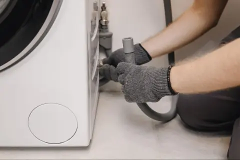 Grijze handschoenen bevestigen een slang aan een wasmachine, mogelijk om wasmachine problemen op te lossen.