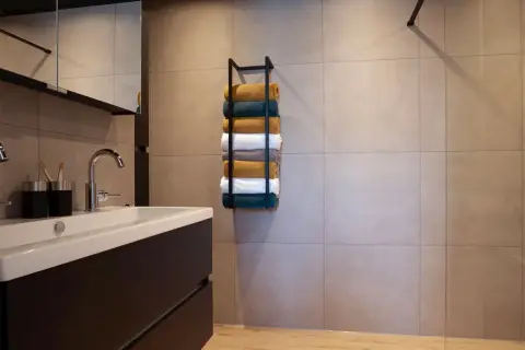 Netjes opgestapelde handdoeken in verschillende kleuren op een zwarte handdoekenrek in een moderne badkamer.