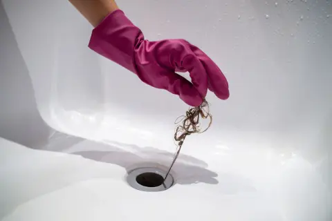 Roze handschoen verwijdert haar uit doucheputje om verstoppingen te voorkomen.