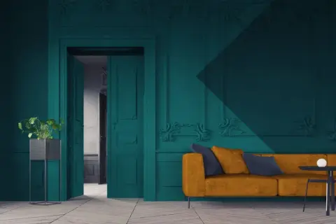 Een modern interieur waar groen en blauw combineren. Een okergele bank met donkerblauwe kussens staat voor een diepblauwe muur met sierlijke ornamenten.