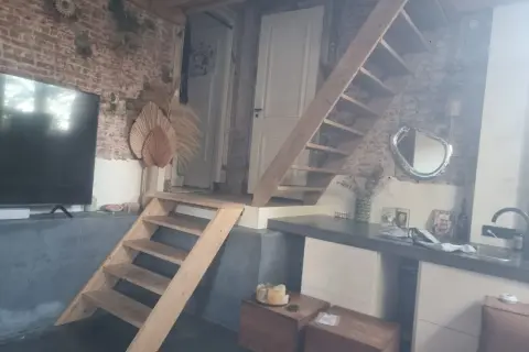 Een vide met een houten trap, bakstenen muur en een tv. Wat is een vide? Een open ruimte in een huis die meerdere verdiepingen verbindt.