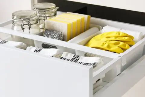 Netjes geordende indeling gootsteenkastje: gele handschoenen, sponzen, schuursponsjes, doekjes en potten met schoonmaakmiddelen.
