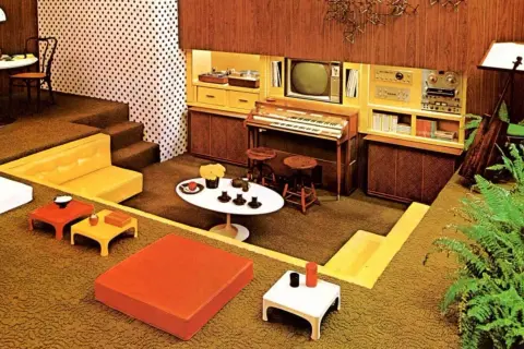 Een retro woonkamer met een **zitkuil jaren 70**, oranje en gele meubels, een orgel en een tv.