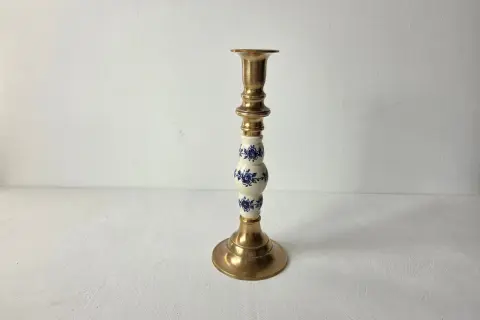 Een gouden kandelaar met een wit porseleinen deel, versierd met blauwe bloemen. Dit is wat vintage is: een stukje geschiedenis dat warmte en sfeer brengt.