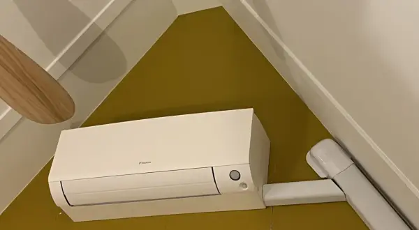 Een witte airco unit met een Daikin logo, netjes gemonteerd. De airco leidingen zijn weggewerkt in witte kokers, wat zorgt voor een strakke afwerking.