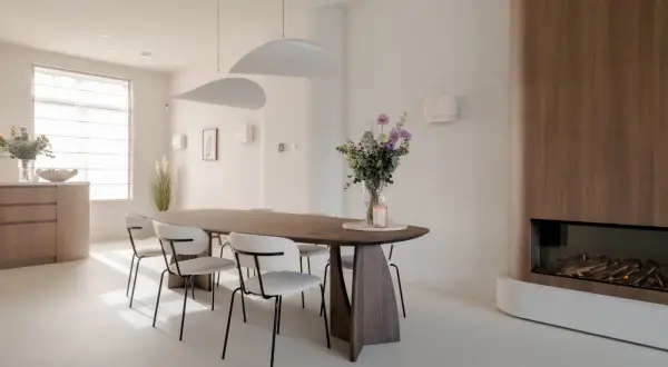 Eettafel met stoelen in een modern, licht interieur. Een vaas met bloemen en een kaars op tafel. Een gashaard met houten ombouw. Dit feng shui huis straalt rust uit.