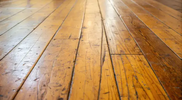 Gouden houten vloer met zichtbare krassen in gelakt hout, die verhalen vertellen van geleefde momenten.