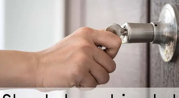 Hand probeert een sleutel in een deurklink te draaien, maar de sleutel zit vast in het slot en draait niet.
