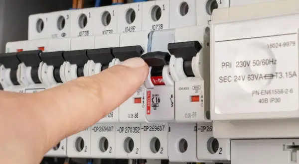 Vinger schakelt een zekering om, mogelijk om een kortsluiting op te sporen in de meterkast.