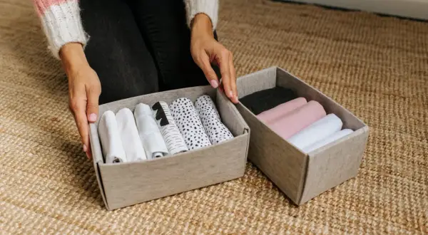 Handen sorteren opgerolde kleding in opbergdozen. Een slimme manier om je huis netjes te houden met deze huishouden tips.