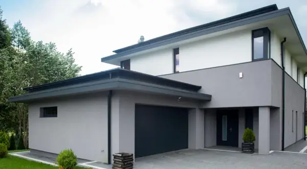 Moderne woning met grijze buiten stuc, donkere garagepoort en entree. Omringd door groen.