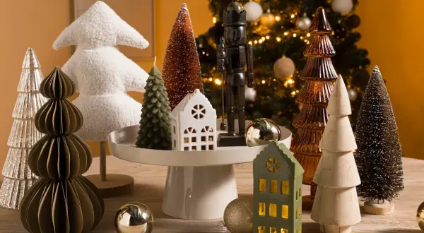 Kerstboom decoratie in Scandinavische stijl: diverse kerstboompjes, een notenkraker en huisjes op een houten tafel.