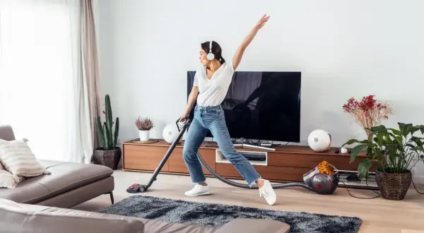 Vrolijke vrouw met koptelefoon danst tijdens de voorjaarsschoonmaak met de stofzuiger.