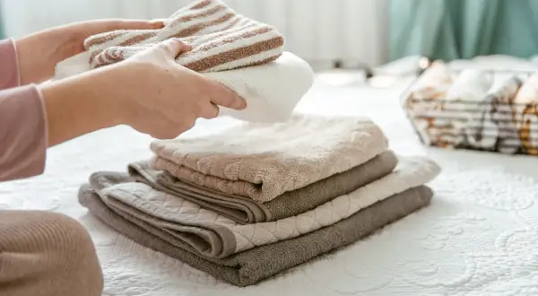 Handen vouwen gestreepte en effen handdoeken. De stapel handdoeken op het bed is zo netjes, dat ze bijna niet drogen.