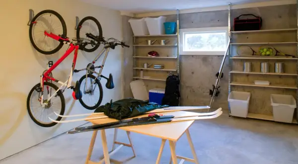 Een opgeruimde kelder met fietsen aan de muur, ski's op een tafel en opbergplanken vol spullen.