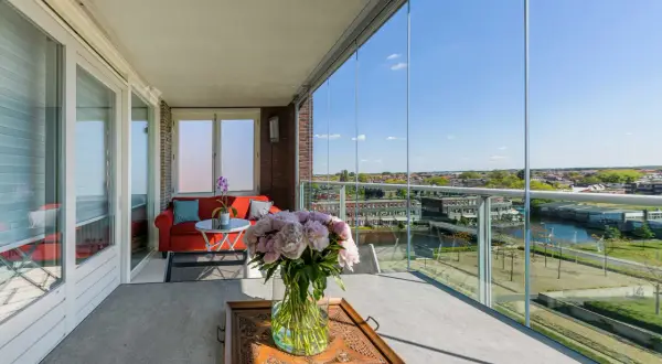 Een prachtig uitzicht vanaf dit balkon, dat met glazen schuifwanden is dichtgemaakt. Een rode bank en bloemen maken het gezellig.