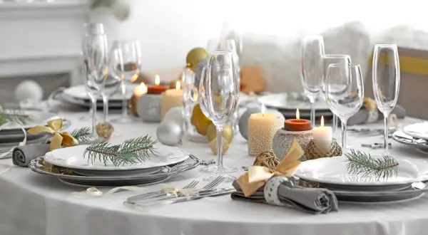 Een feestelijk gedekte tafel met glazen, kaarsen, kerstballen en dennentakjes. Klaar voor een gezellig diner!