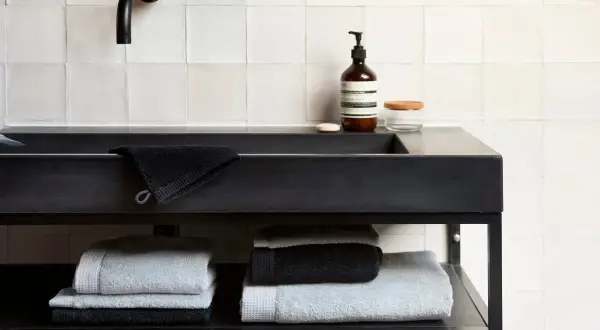 Stapel donkere handdoeken wassen en lichte handdoeken op een plank onder een zwarte wastafel.