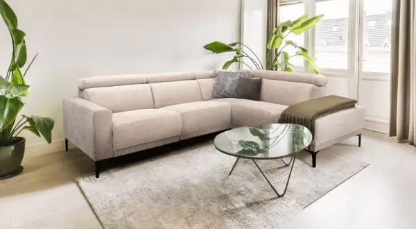 Licht beige hoekbank met kussens en plaid, een marmeren salontafel en grote planten creëren een rustig slow living interieur.
