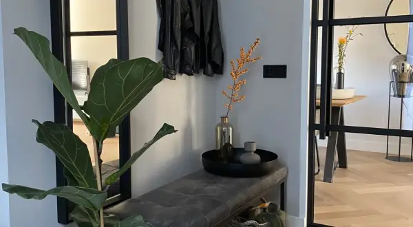 Een mooie hal met een grote plant, leren jasjes aan de kapstok, een bankje en een mand.