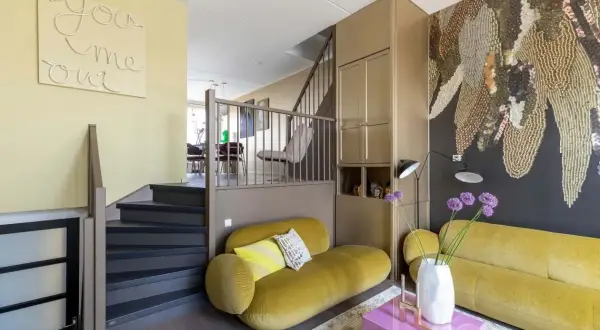 Gezellige split level woning met gele bank, trap en opvallende muurdecoratie.